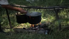 In glade in summer forest, tourists made fire, hung pot over it, cooking food