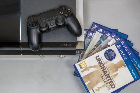 A series of PS4 game covers next to Sony gaming console and DualShock 4 wireless controller with logo. xkwx Playstation 4 games, PS4 games, Playstation 4 game titles, Dualshock 4 wireless, PS4 wireless controller, gaming console, leisure gaming time, play, console, entertainment, technology, fun, gamer, Sony, computer, joy, hobby, button, electronic, toy, digital, fun concept, enjoy, tech, relaxation, fun time, illustrative editorial, recreational, stay at home, disc, hardware, competition, buttons, spare time, accessory, pad, competitive, recreation, touchpad, equipment, creative, digital device