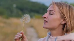 Portrait of a beautiful young blonde woman blowing on the ripened dandelion