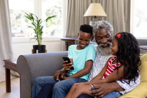 Senior African American man and his grandchildren enjoying their time at home together, sitting on a couch, embracing, smiling, using a smartphone xkwx Three People, Child, Girl, Female, Mixed-Race, Boy, Male, Black, Mid Adult, Man, People, Family, Grandfather, Granddad, Granddaughter, Grandson, Siblings, Brother, Sister, Childhood, Together, Closeness, Interacting, Sitting, Couch, Holding, Using, Phone, Mobile Phone, Smartphone, Connection, Communication, Real People, Home, House, Domestic Life, Lifestyle, Enjoying, Free Time, Leisure, Relaxing, Weekend, Summer, Sunny, Love, Indoors