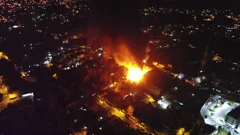 Aerial orbit, drone shot around a burning house. dark smoke and red fire