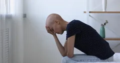 Bald woman sit on bed feels hopeless due cancer disease