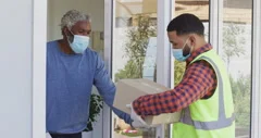 Delivery man delivering package to senior man wearing face mask at home