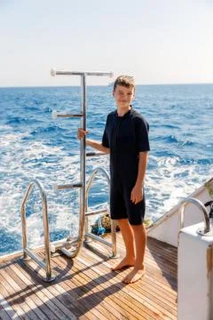 A 14-year-old boy in a diving suit stands on the stern of a yacht Stock Photos