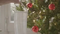 A White Face Mask Is Hung On A Xmas Tree Over A Blurred Background For Covid Chr