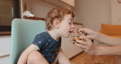 1.5 year old boy eats kiwi using a spoon. mom helps baby Stock Footage 117103274