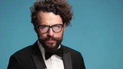curly hair guy in elegant tuxedo with glasses adjusting and fixing moustache,