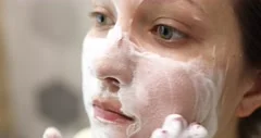 Young woman is washing applying foam cleanser on face. Daily facial skincare