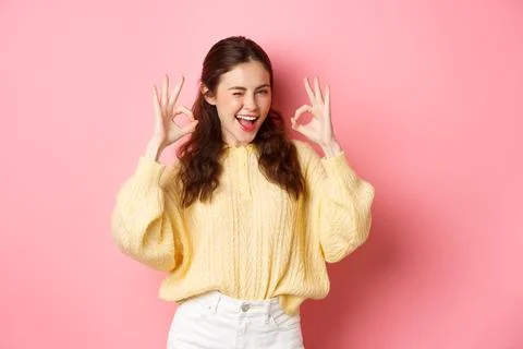 Portrait of cheerful pretty girl winking and saying yes, showing okay sign, alright gesture, praise good job, well done, standing pleased against pink background. xkwx student, girl, background, okay, good, approve, alright, agree, yes, praise, woman, advertising, fashion, beauty, person, portrait, grinning, joy, pink, beautiful, joyful, pleased, positive, smile, stylish, studio, horizontal, young, gesturing, glamour, holiday, excited, shopping, isolated, adult, girlfriend, advertisement, casual, smiling, emotive, slim, upbeat, glamorous, cheerful, emotions, excitement, fashionable, brunette