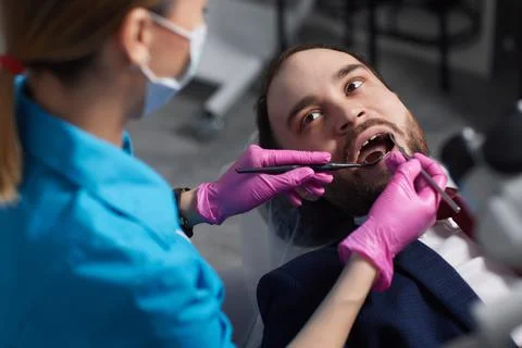 Smiling young man sitting in dentist chair while doctor examining his teeth xkwx {medical,woman,man,doctor,dentist,tool,specialist,procedure,patient,oral,gloves,examination,health,treatment,clinic,tooth,teeth,dental,medicine,caucasian,equipment,stomatology,visit,mouth,cabinet,checkup,cure,examine,young,uniform,surgical,protective,mask,toothache,latex,operation,hygiene,orthodontist,occupation,dentistry,workplace,indoors,instrument,sterile,heal,hospital,inspection}