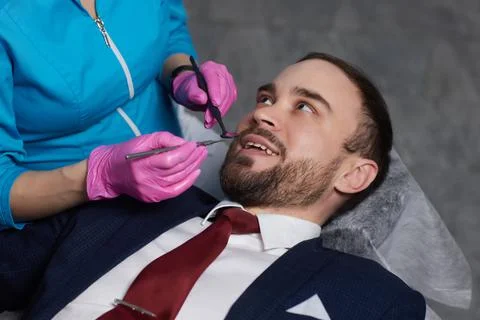 Smiling young man sitting in dentist chair while doctor examining his teeth xkwx {medical,woman,man,doctor,dentist,tool,specialist,procedure,patient,oral,gloves,examination,health,treatment,clinic,tooth,teeth,dental,medicine,caucasian,equipment,stomatology,visit,mouth,cabinet,checkup,cure,examine,young,uniform,latex,indoors,orthodontist,sterile,protective,mask,dentistry,hospital,toothache,surgical,instrument,hygiene,workplace,heal,operation,inspection,occupation}