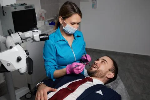 Smiling young man sitting in dentist chair while doctor examining his teeth xkwx {medical,woman,man,doctor,dentist,tool,specialist,procedure,patient,oral,gloves,examination,health,treatment,clinic,tooth,teeth,dental,medicine,caucasian,equipment,stomatology,visit,mouth,cabinet,checkup,cure,examine,young,uniform,surgical,protective,mask,toothache,latex,operation,hygiene,orthodontist,occupation,dentistry,workplace,indoors,instrument,sterile,heal,hospital,inspection}