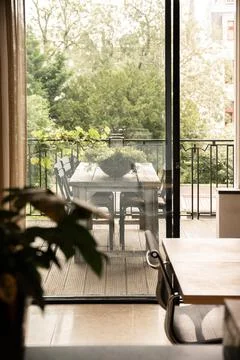 Wooden  table  and  flower  in  light  room  near  transparent  door  of  terrace  with  wooden  table  and  green  plant  near  fence  and  trees  in  city xkwx {{table,terrace,room,style,interior,design,plant,decor,flower,veranda,apartment,door,transparent,potted,entrance,leaf,dwell,decoration,fence,wooden,light,home,summer,tree,domestic,chair,seat,creative,flat,residential,flowerpot,green,modern,estate,material,glass,property,floral,clean,part,fencing,barrier,vertical,inside}}