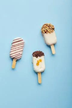 Mousse  dessert  with  fruit  flavors  in  the  form  of  popsicle  ice  cream  covered  with  white  chocolate  on  blue  background. xkwx ice  cream,  sweet,  mousse,  dessert,  delicious,  food,  cream,  popsicle,  homemade,  lollipop,  cold,  sugar,  stick,  pastry,  party,  pop,  shape,  vanilla,  tasty,  sprinkle,  fruit,  glac,  inside,  flake,  variety,  copy,  cupcake,  filling,  space,  stacked,  assortment,  bright,  cheesecake,  nobody,  closeup,  cookie,  fresh,  plate,  cool,  chocolate,  decoration,  cake,  gastronomy,  meal