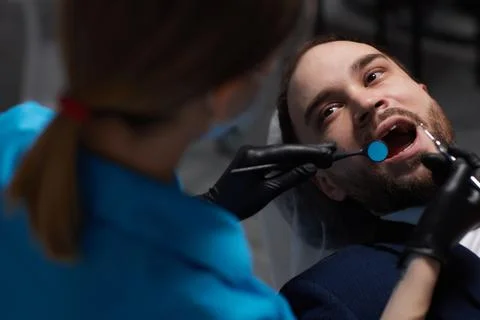Smiling young man sitting in dentist chair while doctor examining his teeth xkwx medical, woman, man, doctor, dentist, tool, specialist, procedure, patient, oral, gloves, examination, health, treatment, clinic, tooth, teeth, dental, medicine, caucasian, equipment, stomatology, visit, mouth, cabinet, checkup, cure, examine, young, uniform, surgical, protective, mask, toothache, latex, operation, hygiene, orthodontist, occupation, dentistry, workplace, indoors, instrument, sterile, heal, hospital, inspection