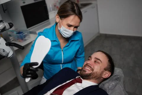 Smiling young man sitting in dentist chair while doctor examining his teeth xkwx medical, woman, man, doctor, dentist, tool, specialist, procedure, patient, oral, gloves, examination, health, treatment, clinic, tooth, teeth, dental, medicine, caucasian, equipment, stomatology, visit, mouth, cabinet, checkup, cure, examine, young, uniform, surgical, protective, mask, toothache, latex, operation, hygiene, orthodontist, occupation, dentistry, workplace, indoors, instrument, sterile, heal, hospital, inspection
