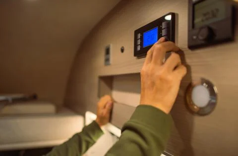 Caucasian Men Adjusting Interior RV Camper Van Temperature. Modern Motorhome Heating and Cooling Technologies. xkwx temperature,rv,motorhome,motor coach,camper van,camping,rv park,heat,cool,air conditioning,air ventilation,adjusting,adjust,touch,controller,control,interior,inside,technology,electronic