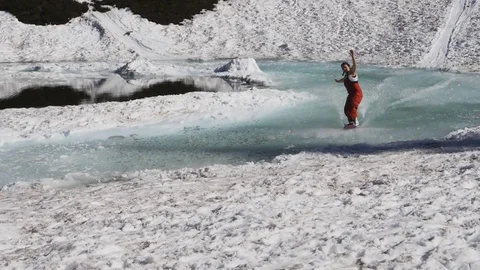 180p slow motion tracking shot of a female snowboarder crossing a slushy pond Stock Footage 98918397