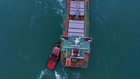 19.0Da red tugs pushing a large green ship with a helipad on the water seam of Video stock 129617427