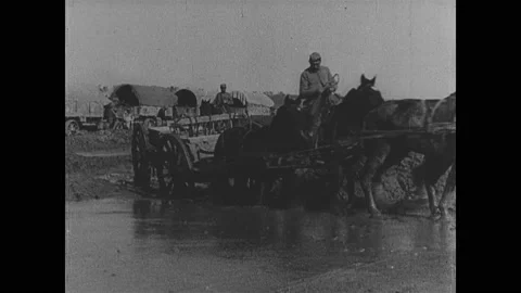 1910s: Men riding horses pulling cart across muddy water, wagon train in Video stock 148225897