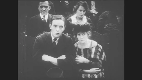 1910s: Young couple watches a movie in a theater, they watch the screen with Stock Footage
