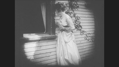 1910s: Young woman worriedly looks through window at man lying on floor. Stock Footage