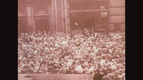 1920s: Large street crowd cheers and waves hats. People in balconies wave flags. Stock Footage