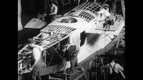 1920s: Men construct military bi-planes. Crane carries plane body across factory Stock Footage 98523656