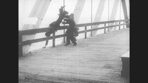 1920s: men tumble on bridge to avoid police car. old woman waves gun. man in Video stock 76751271