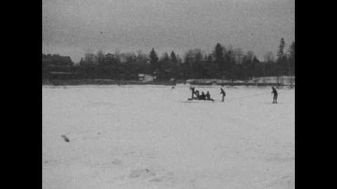 1920s: Sled with engine and propeller pulls two people on skis across snow. Stock Footage 126008494