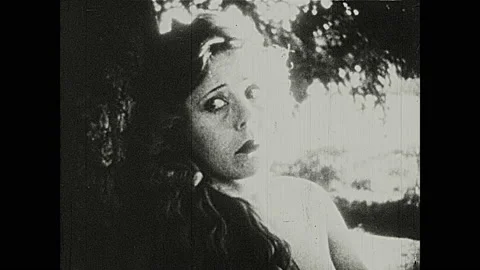 1920s: Snake curls around tree branch. Woman leans against tree and looks up. Stock Footage 149772097