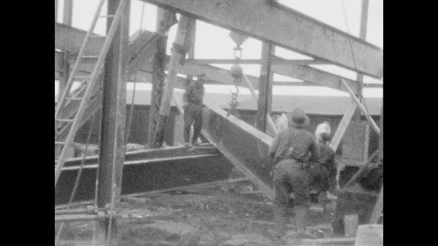 1920s: UNITED STATES: men build steel frame on construction site. Men guide beam Stock Footage