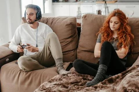Full body of sad redhead female sitting on comfortable couch near boyfriend playing interesting videogame in light living room at home xkwx couple, videogame, bored, ignore, pastime, leisure, relationship, play, hobby, sad, together, home, spend time, upset, boyfriend, girlfriend, apartment, light, man, woman, flat, at home, soulmate, entertain, boredom, partner, sofa, living room, couch, headphones, game, weekend, free time, gamepad, chill, problem, gamer, player, frustrate, settee, trouble, disappoint, inside, full body, redhead, ginger, long hair, red hair