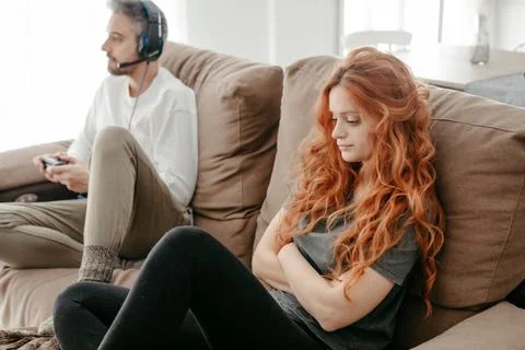 Full body of sad redhead female sitting on comfortable couch near boyfriend playing interesting videogame in light living room at home xkwx couple, videogame, bored, ignore, pastime, leisure, relationship, play, hobby, sad, together, home, spend time, upset, boyfriend, girlfriend, apartment, light, man, woman, flat, at home, soulmate, entertain, boredom, partner, sofa, living room, couch, headphones, game, weekend, free time, gamepad, chill, problem, gamer, player, frustrate, settee, trouble, disappoint, inside, redhead, ginger, long hair, red hair