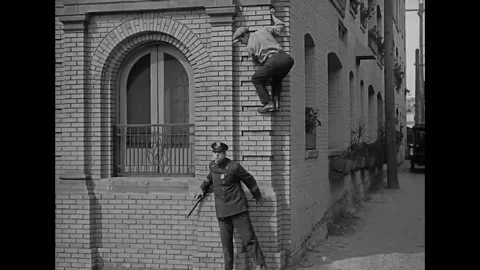 1923 - In this silent comedy, a man climbs up the side of a building to escape a Stock Footage 205512215