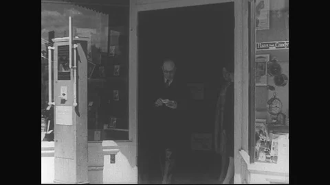 1929: Several customers and employees walk in and out of a shop entrance. Two Stock Footage