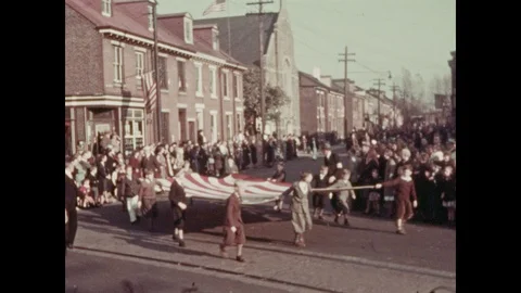 1930s: Children hold on to giant American flag, march down street. Men in Stock Footage