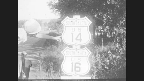 1930s: Girl In Parked Car Points To Road Signs: South Dakota Us 14 And Us 16. Stock Footage