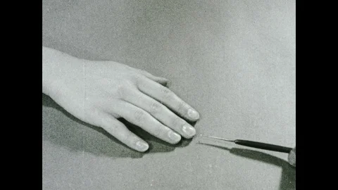 1930s: Hand with sharpened pointer pokes woman's hand. Woman's hand jerks back. Video stock 104992317