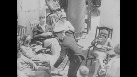1930s: Man serves tea to men and women on deck of ship. Large ocean liner steams Stock Footage 81896366