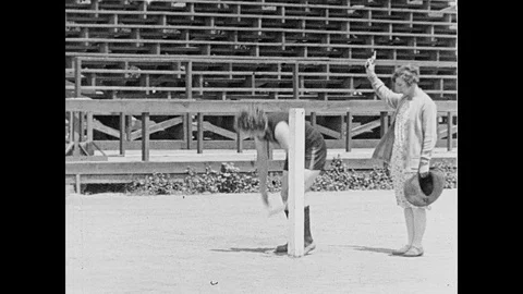 1930s: A relay runner crouches at the start of the course. Her coach fires a Stock Footage 95351126