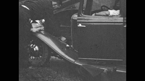 1930s: Three men look over a map. One man checks the engine of a car, another Video stock 236169676