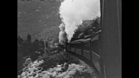 1930s: Train goes down tracks. River goes through valley in the mountains. Stock Footage