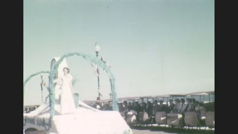 1930s: Two women in dresses/gowns ride a white and green parade float. A large Stock Footage