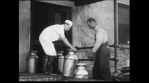 1930s: Wide shot of milkman handing milk cannisters to dock worker or customer Stock Footage