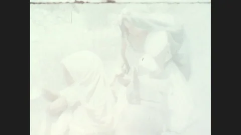 1930s: Woman with blanket on her head kneeling in a dusty road. Sun shines Stock Footage