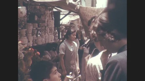 1930s: Woman stands in front of outdoor market stall with shelves of pottery. Stock Footage