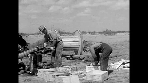 1938 - Men stuff nitroglycerine into casing to go underground by an oil rig. Video stock 92628351