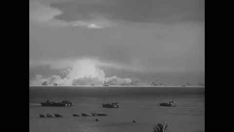 1940s: Atomic bomb explodes on island. Mushroom cloud ascends into sky. Ships in Video stock 159174541
