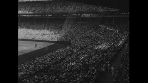 1940s: Baseball stadium.  Spectators sit and stand.  Players run onto field.  Stock Footage 122514571